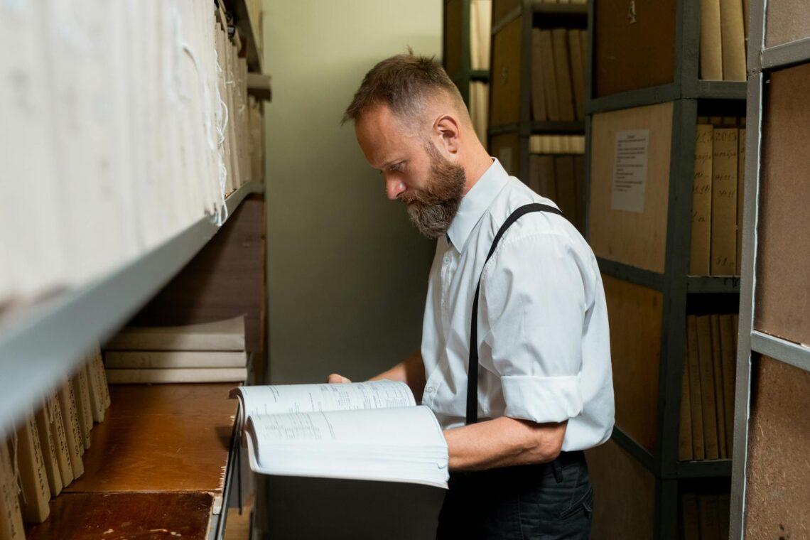 a man wearing white long sleeves with suspenders reading a book